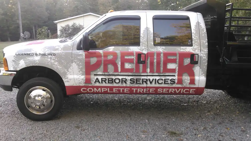 Premier Arbor Services dump-bed truck with the red PREMIER wrap, Complete Tree Service and Licensed & Insured on the door
