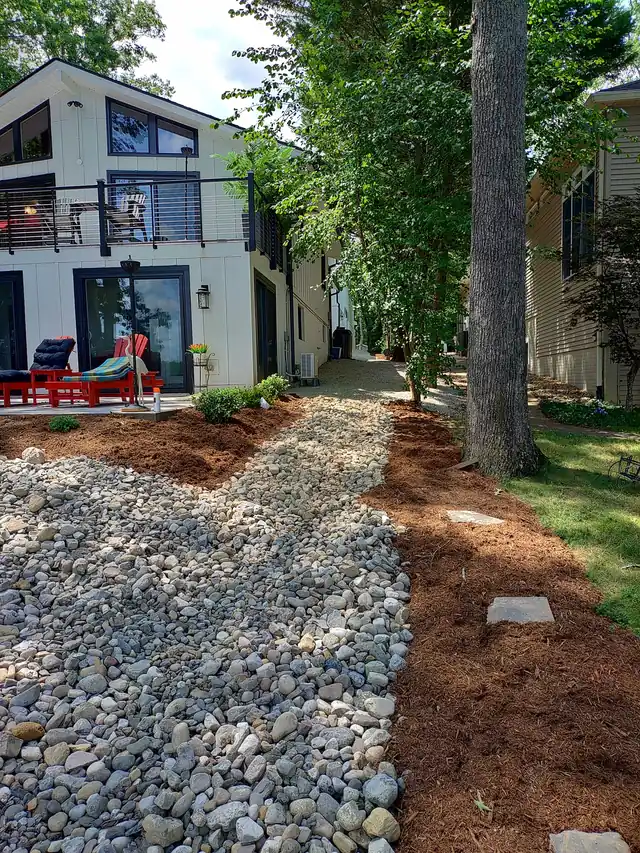 River-rock dry creek bed edged with fresh mulch running down beside a lake house
